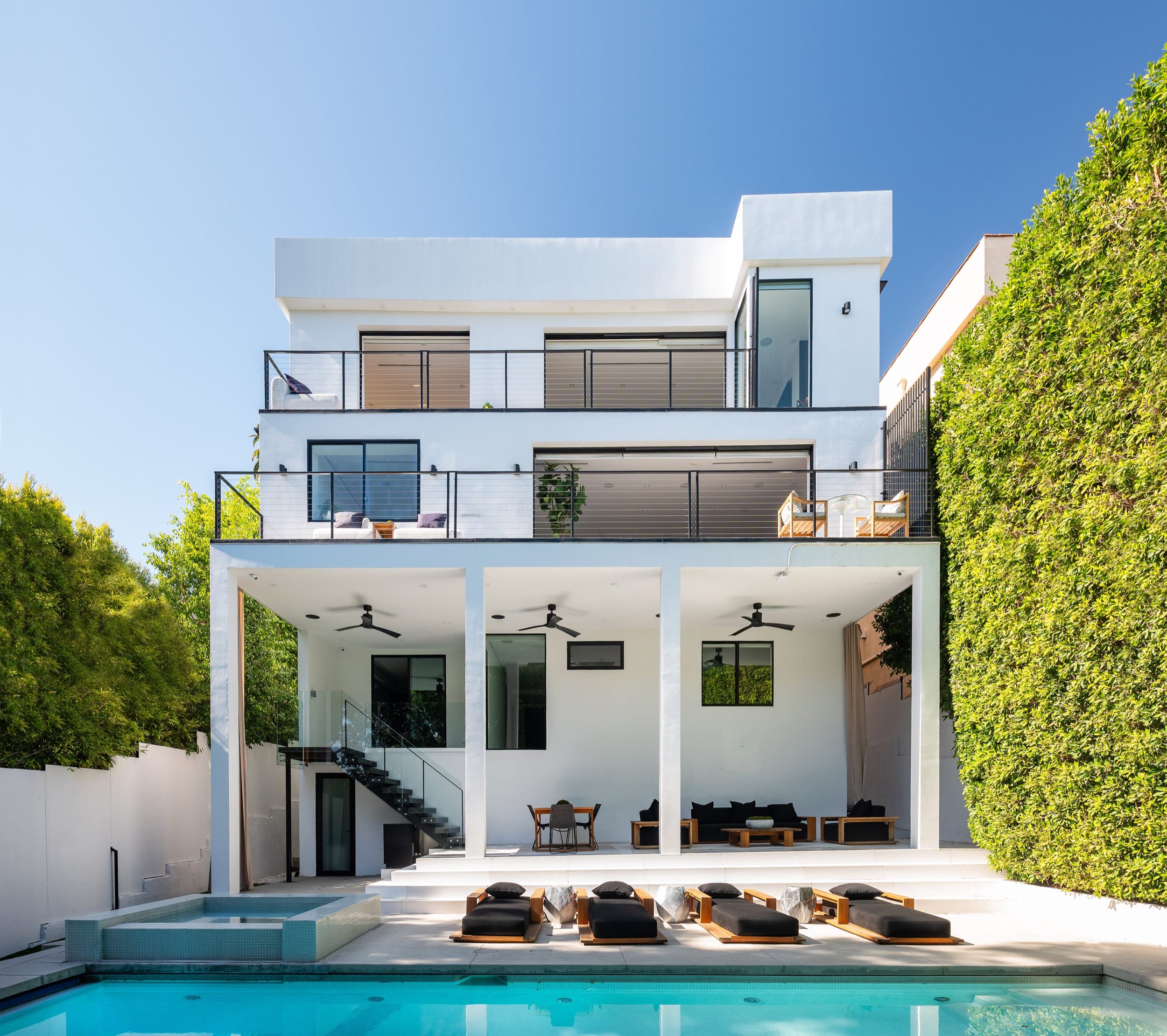 Rear elevation in daylight: covered patio at pool level with terraces off the main level and primary suite above