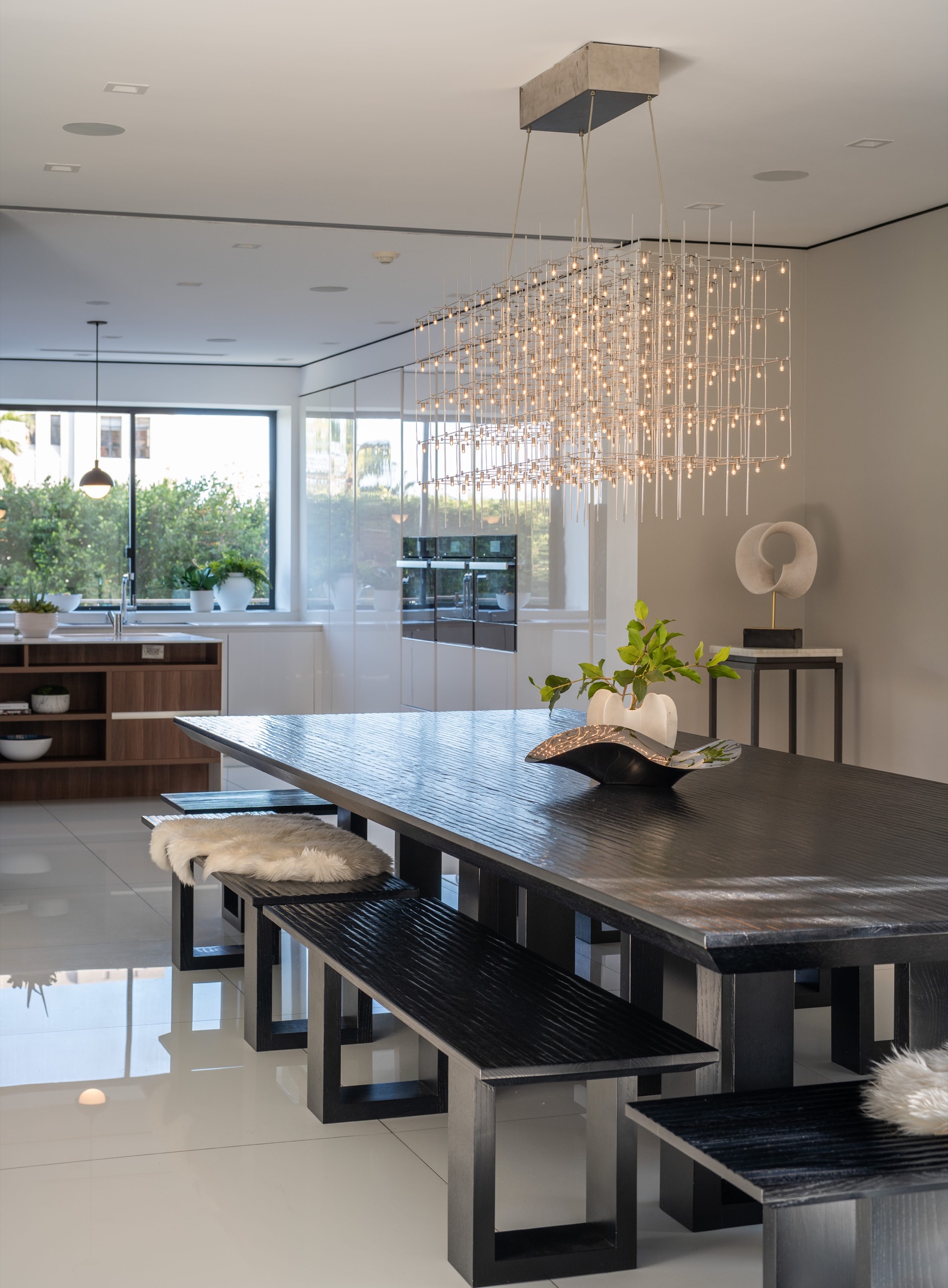 Dining table under the linear chandelier with glass to the terrace