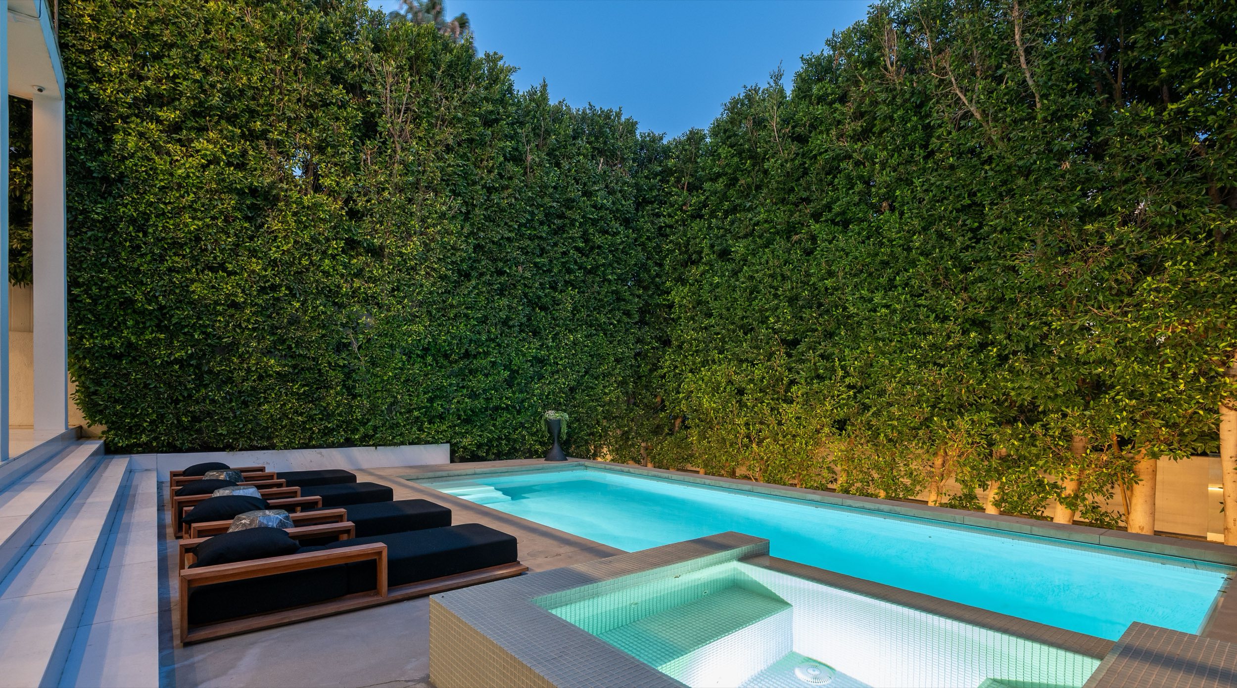 Pool and spa at dusk with the hedge lit behind