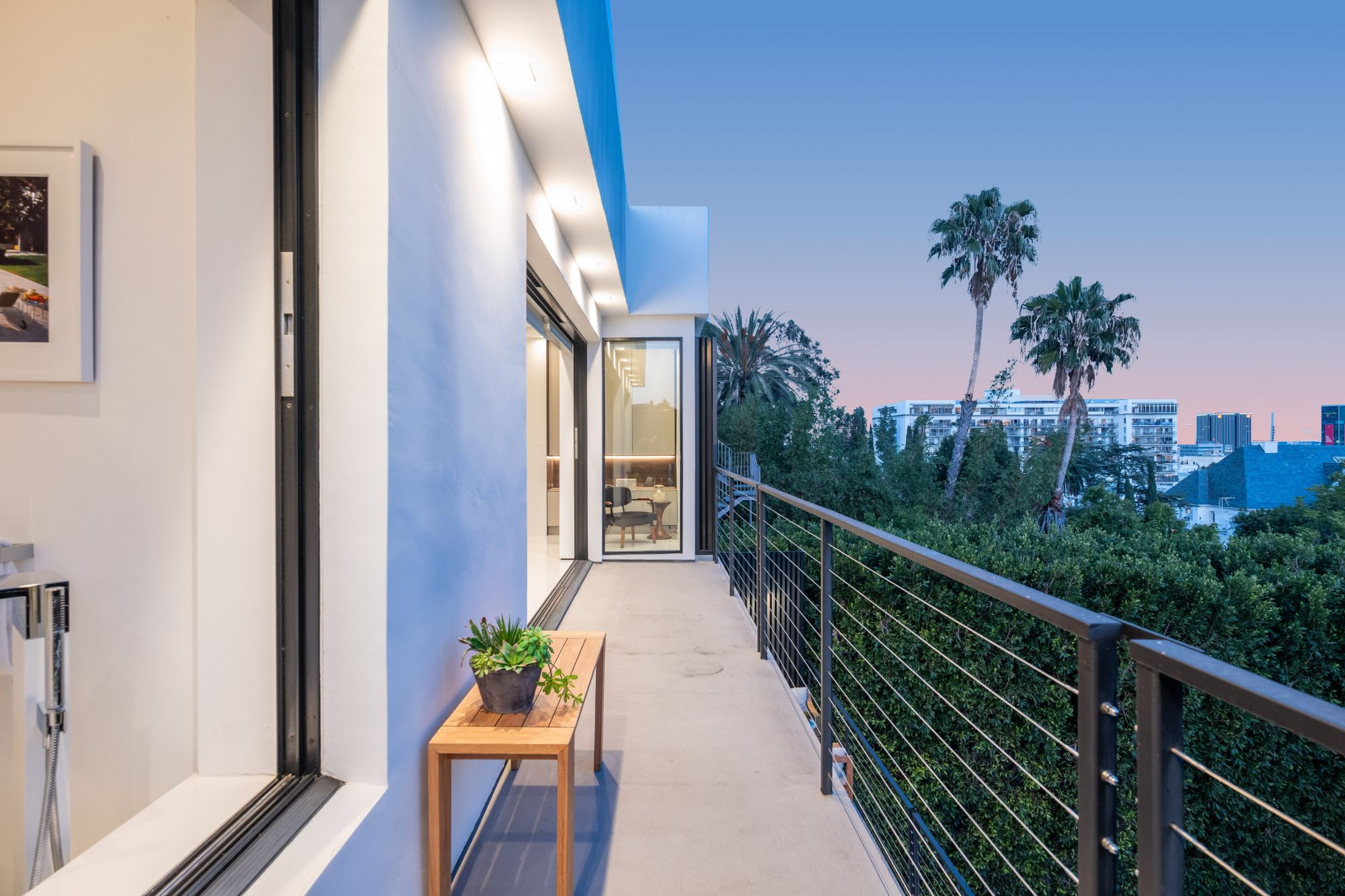 Terrace running along the primary suite at dusk, cable rail above the garden