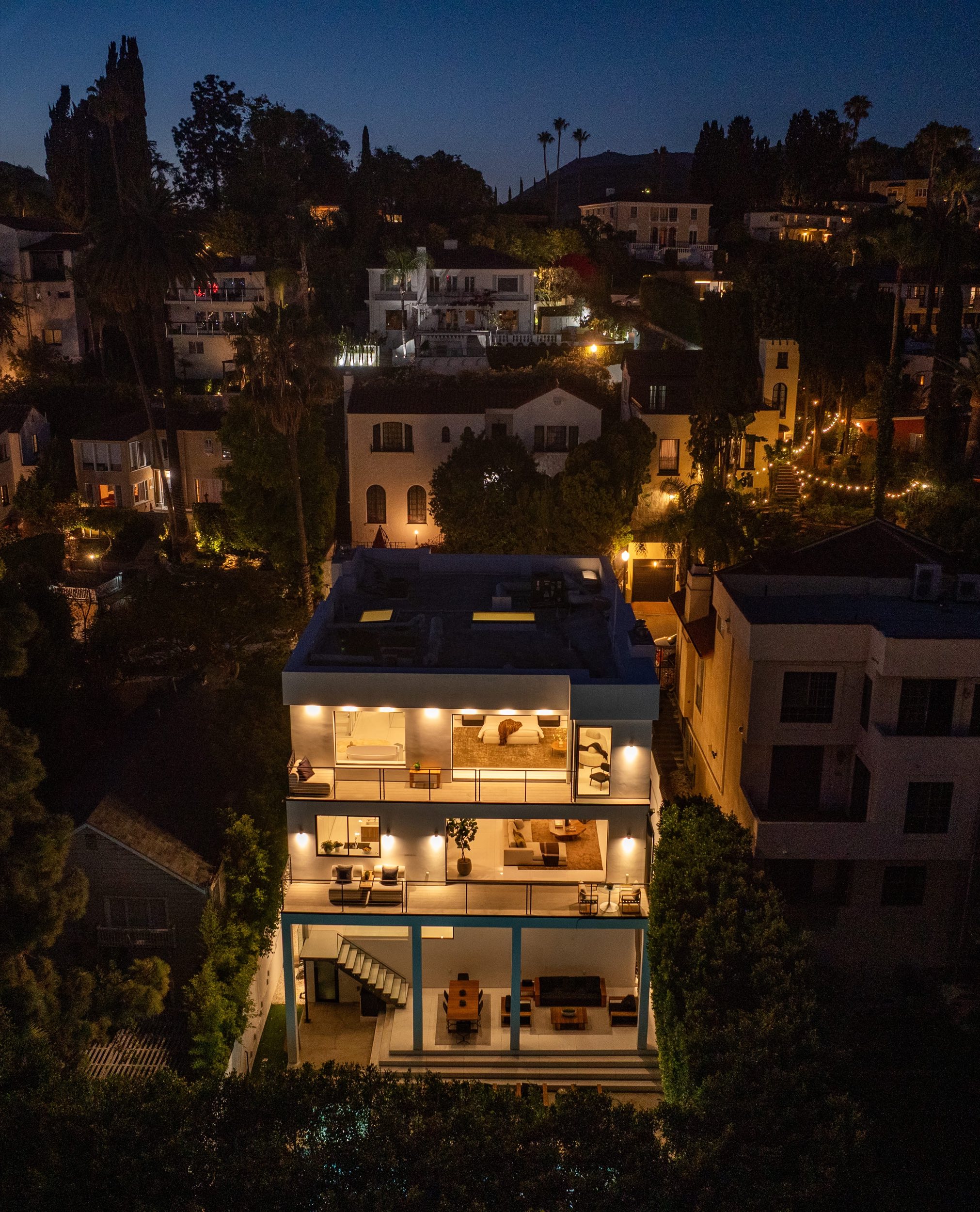 The street and the house from the air at dusk, city lights beyond