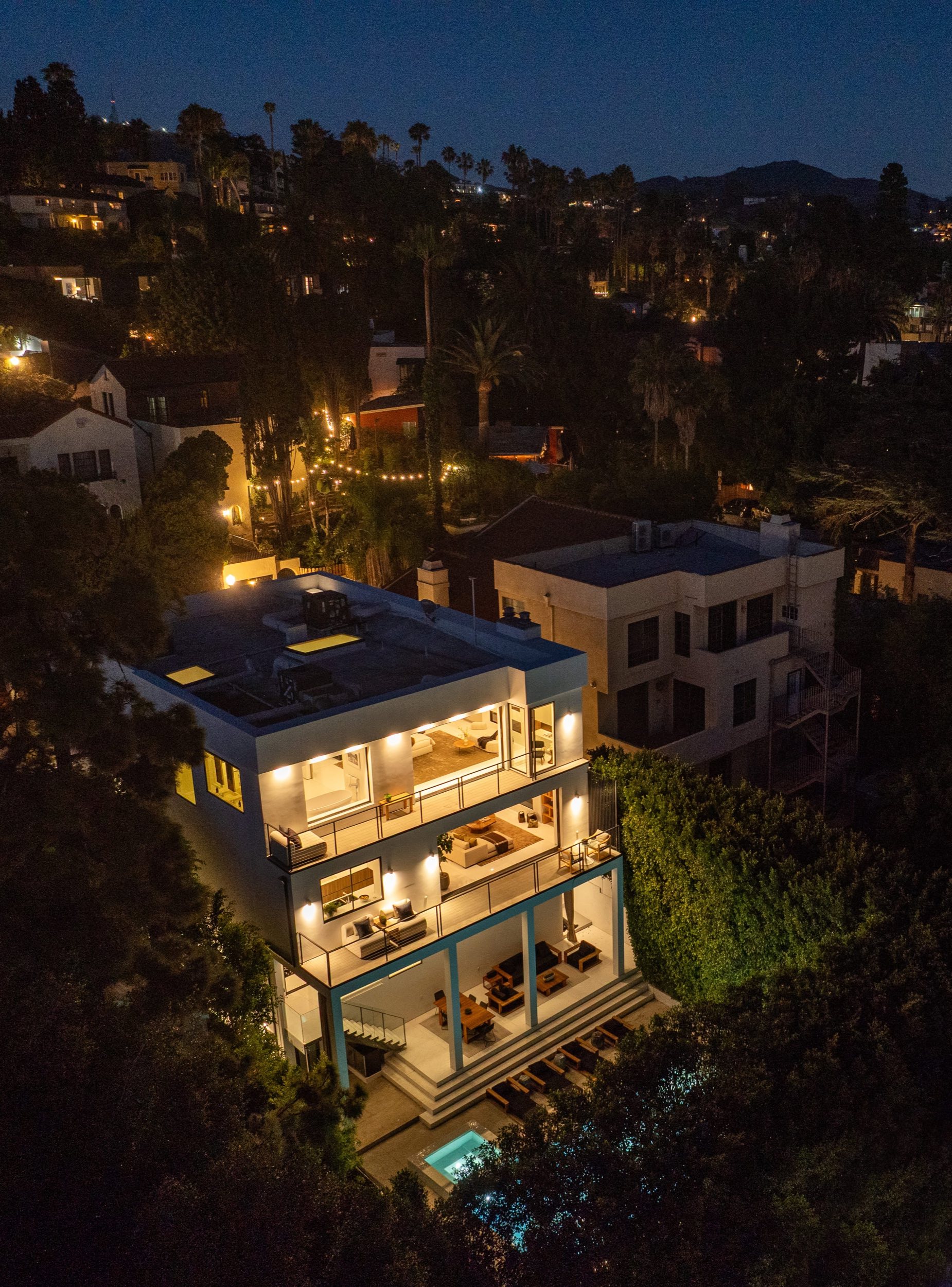 Aerial view at dusk: three lit levels stepping down to the pool